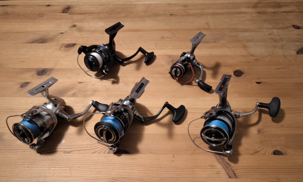 5 spinning reels on a wooden table.