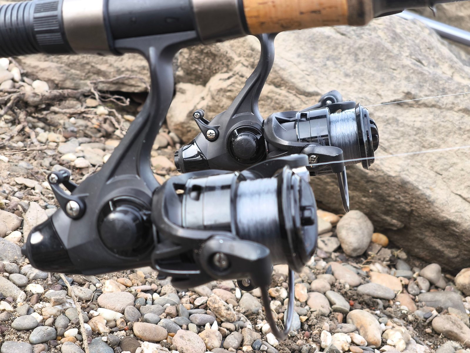 Two baitrunner reels mounted on carbon fiber fishing rods positioned on a rod pod at a lakefront, showcasing the secondary drag system for live bait fishing.